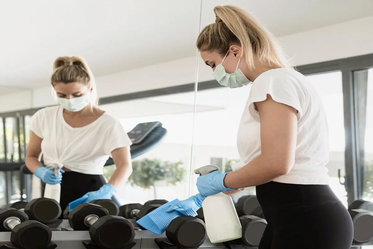 Professional fitness center cleaning service disinfecting gym dumbbells and equipment.